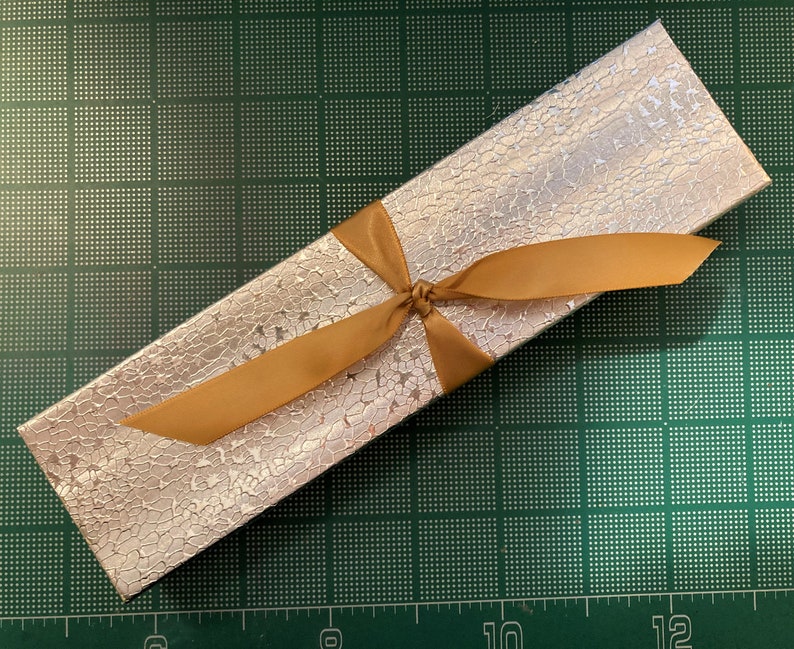 May include: A silver gift box with a gold ribbon tied in a bow. The box has a textured surface.