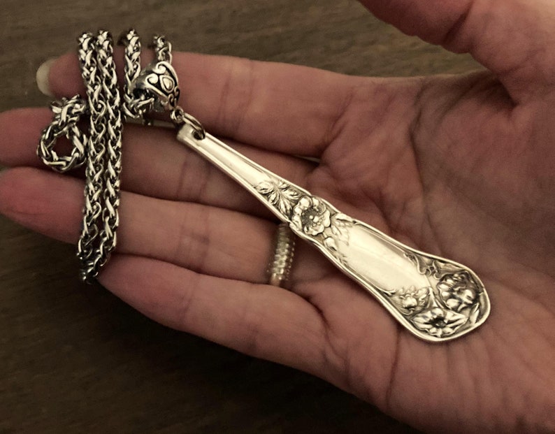 May include: A silver spoon necklace with a floral design. The spoon is attached to a silver chain.