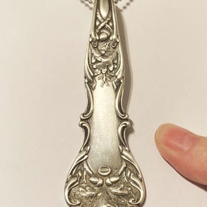 May include: A silver necklace with an ornate pendant featuring an oak leaf design. The pendant is made from a repurposed antique spoon.