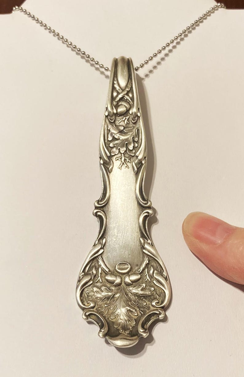 May include: A silver necklace with an ornate pendant featuring an oak leaf design. The pendant is made from a repurposed antique spoon.