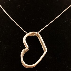 May include: A silver heart-shaped pendant necklace with a delicate chain. The pendant is made of two pieces of metal that are joined together to form a heart shape.