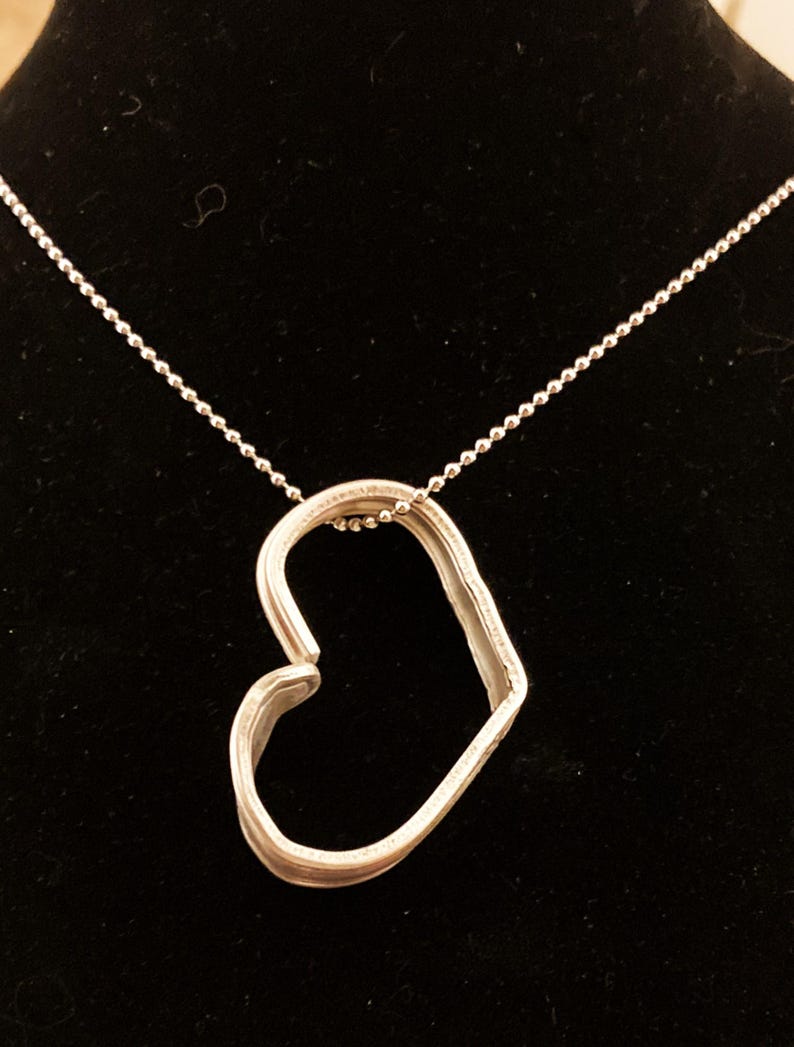 May include: A silver heart-shaped pendant necklace with a delicate chain. The pendant is made of two pieces of metal that are joined together to form a heart shape.
