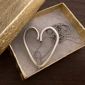 May include: A silver heart-shaped pendant necklace with a silver ball chain in a gold gift box.