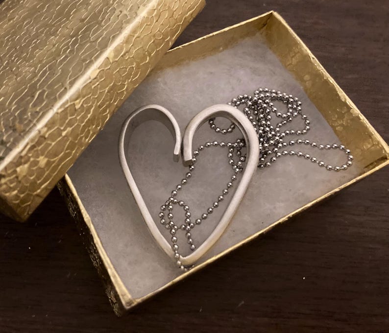 May include: A silver heart-shaped pendant necklace with a silver ball chain in a gold gift box.