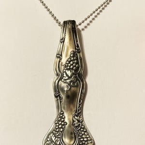 May include: A silver necklace with a pendant made from a vintage spoon. The spoon is decorated with a grapevine design.