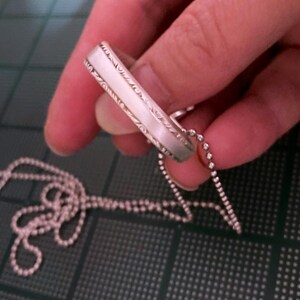 Puede incluir: Un collar de cadena de plata con un colgante de anillo de plata. El anillo tiene un dise&ntilde;o decorativo en el exterior.