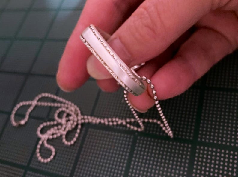 Puede incluir: Un collar de cadena de plata con un colgante de anillo de plata. El anillo tiene un dise&ntilde;o decorativo en el exterior.