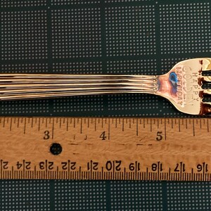 May include: A gold-colored fork with a ribbed handle and a ruler for scale. The ruler is marked with inches.
