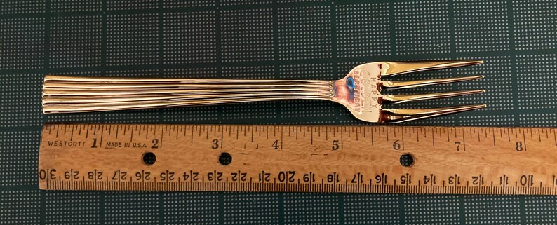 May include: A gold-colored fork with a ribbed handle and a ruler for scale. The ruler is marked with inches.