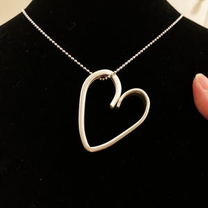 May include: A silver necklace with a heart-shaped pendant. The pendant is made of a single piece of metal that is bent into a heart shape.