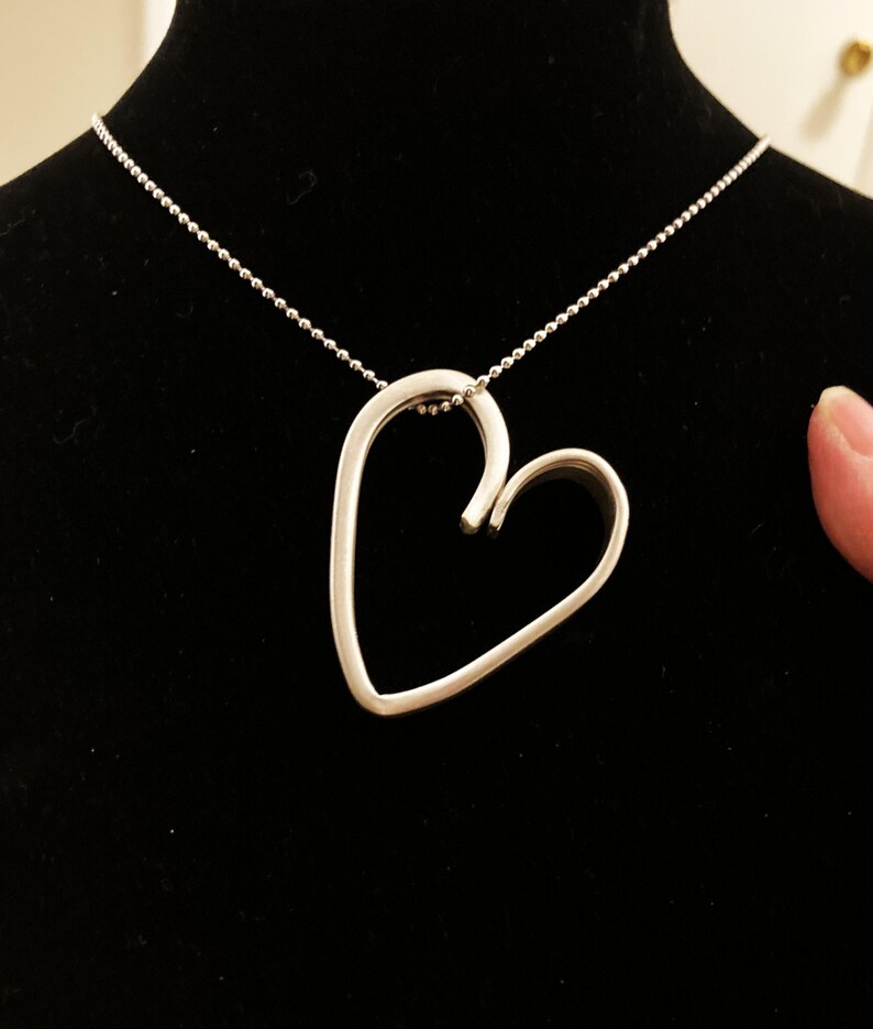 May include: A silver necklace with a heart-shaped pendant. The pendant is made of a single piece of metal that is bent into a heart shape.