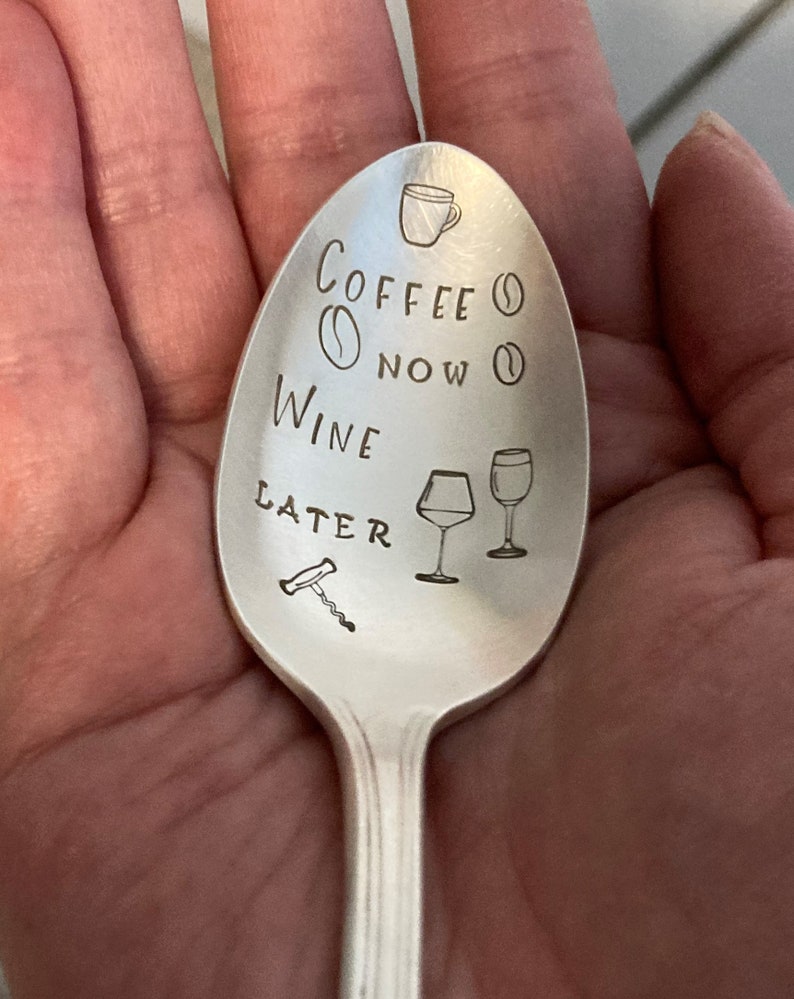 May include: A silver spoon with the text "Coffee Now Wine Later" engraved on it. The spoon also has a small coffee cup, coffee bean, wine glass, and corkscrew engraved on it.