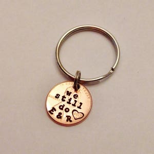 May include: A copper penny keychain with the words "We still do" and a heart with the letters "F & R" engraved on it.