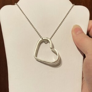Puede incluir: Un collar de plata con un colgante en forma de coraz&oacute;n. El colgante est&aacute; hecho de una sola pieza de metal que se dobla en forma de coraz&oacute;n. La cadena es una cadena de bolas simple.