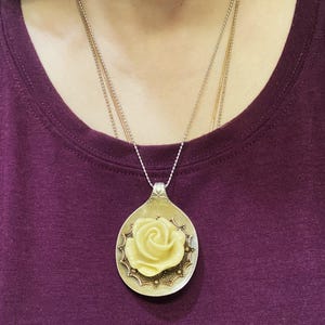 May include: A silver spoon pendant necklace with a yellow rose design. The spoon is decorated with a gold-colored border and small gold dots.