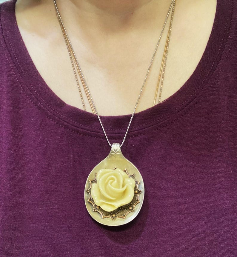 May include: A silver spoon pendant necklace with a yellow rose design. The spoon is decorated with a gold-colored border and small gold dots.
