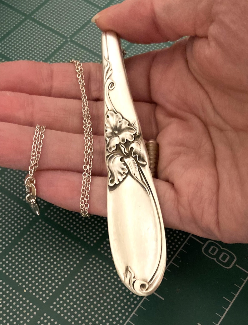 Puede incluir: Collar con colgante de cuchara de plata con detalles florales. El colgante es una cuchara reutilizada con una delicada cadena. La cuchara presenta un dise&ntilde;o floral en relieve. El collar es una joya &uacute;nica.