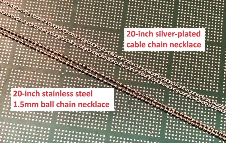 May include: Two silver chains on a green background. The top chain is a 20-inch silver-plated cable chain necklace. The bottom chain is a 20-inch stainless steel 1.5mm ball chain necklace.