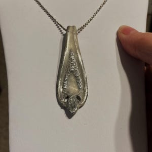 May include: A silver necklace with a pendant made from a vintage silverware spoon. The spoon has an ornate design with floral details.