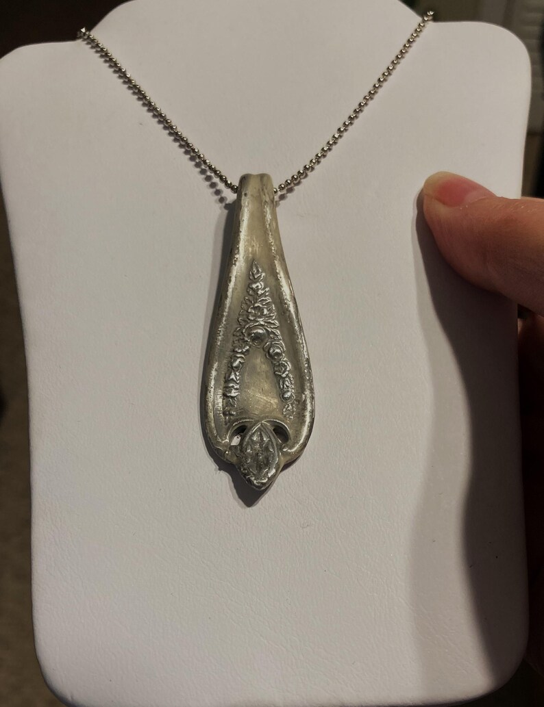 May include: A silver necklace with a pendant made from a vintage silverware spoon. The spoon has an ornate design with floral details.