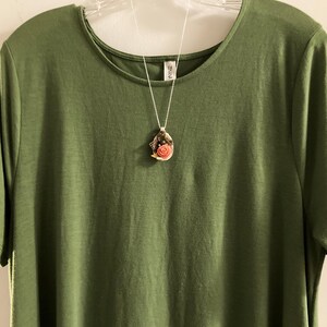 May include: A green t-shirt with a silver chain necklace featuring a seashell pendant with a pink flower inside.