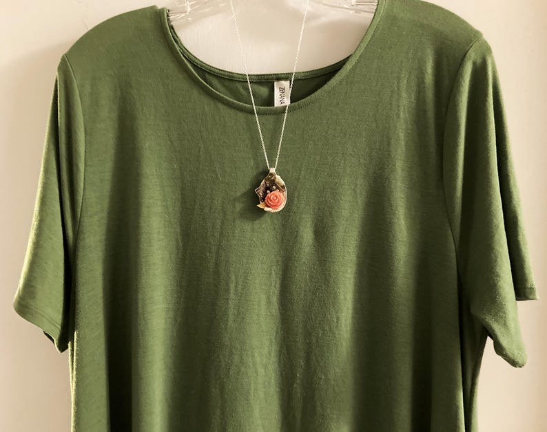 May include: A green t-shirt with a silver chain necklace featuring a seashell pendant with a pink flower inside.