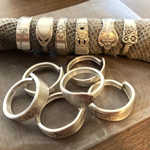 Puede incluir: Un juego de diez anillos de servilleta de plata hechos con cubiertos reutilizados. Los anillos est&aacute;n decorados con motivos florales y tienen un acabado pulido.