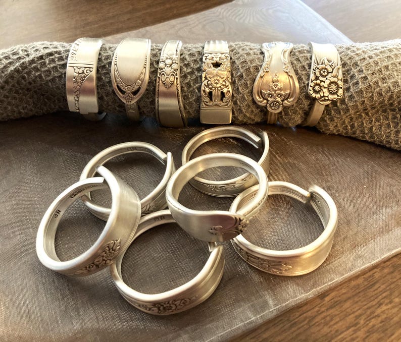 Puede incluir: Un juego de diez anillos de servilleta de plata hechos con cubiertos reutilizados. Los anillos est&aacute;n decorados con motivos florales y tienen un acabado pulido.
