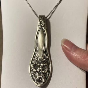 May include: A silver necklace with a pendant made from a vintage spoon. The spoon is decorated with a floral design.