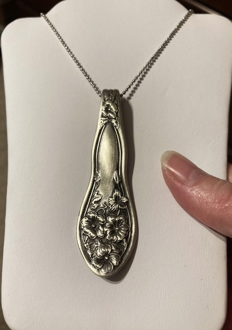 May include: A silver necklace with a pendant made from a vintage spoon. The spoon is decorated with a floral design.
