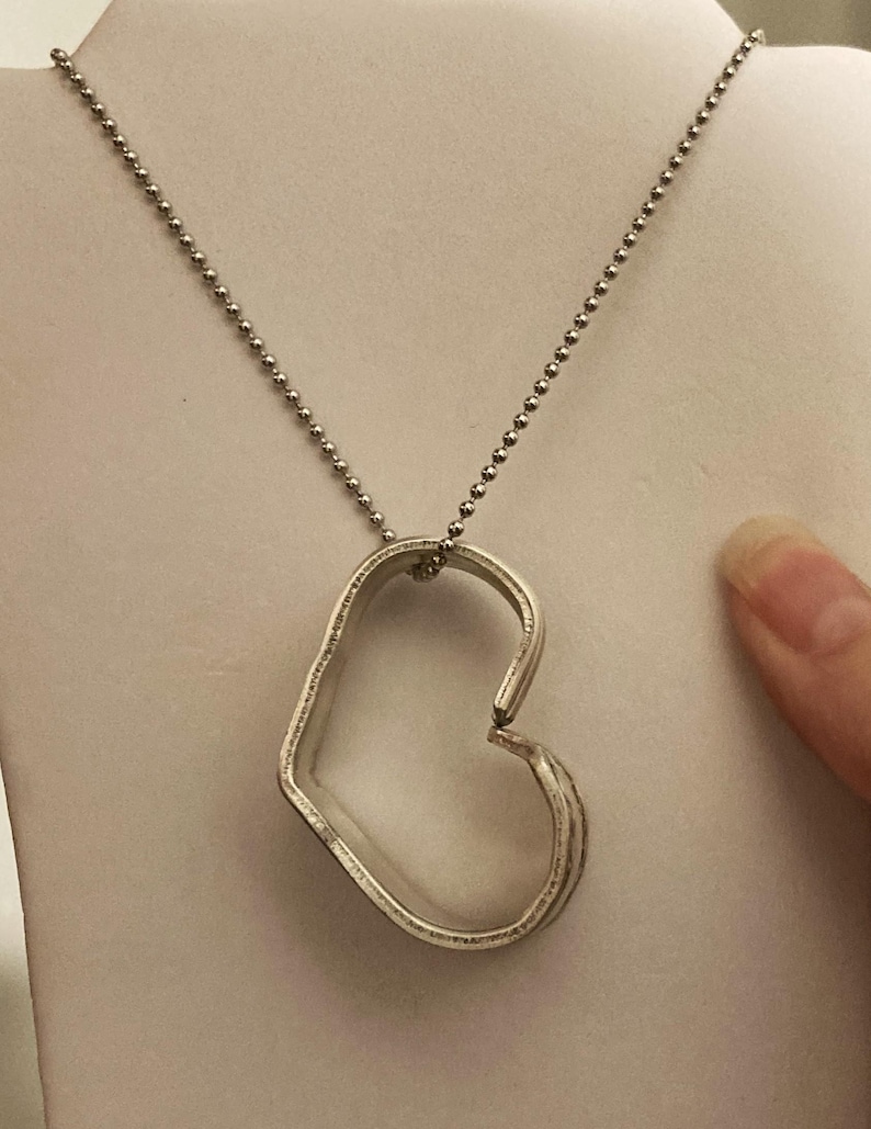 May include: A silver necklace with a heart-shaped pendant. The pendant is made of metal and has a slightly open design.