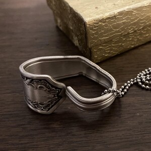 May include: A silver spoon ring with an ornate design and a silver chain attached.