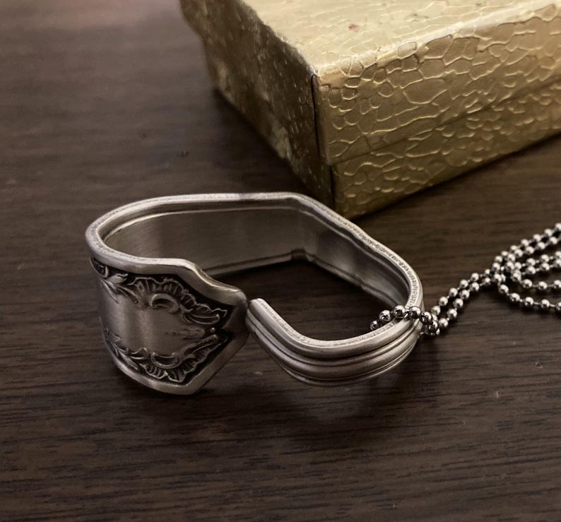 May include: A silver spoon ring with an ornate design and a silver chain attached.