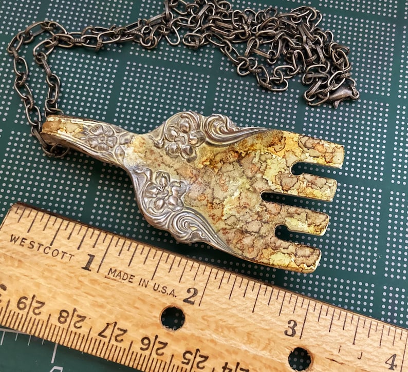 May include: A silver-tone necklace with a decorative fork pendant. The fork is ornate with floral details and has a gold-tone finish. The necklace is approximately 18 inches long.