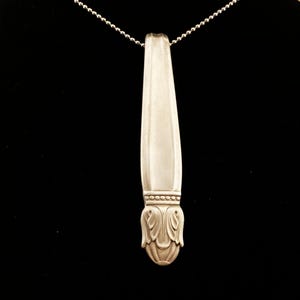 May include: A silver spoon pendant necklace with a decorative floral design at the bottom. The spoon is attached to a silver ball chain.