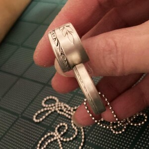 May include: A silver pendant necklace with a detailed floral design. The pendant is made of two pieces that fit together. The necklace is on a silver ball chain.