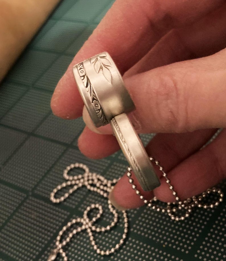 May include: A silver pendant necklace with a detailed floral design. The pendant is made of two pieces that fit together. The necklace is on a silver ball chain.