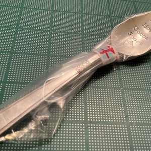 May include: A silver spoon with the words "My Hot Cocoa Spoon" engraved on the bowl. The spoon is wrapped in clear plastic and tied with a red and white ribbon.