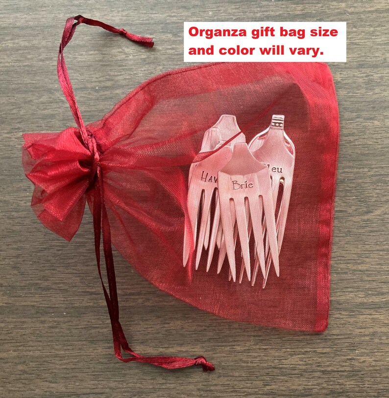 May include: A red organza gift bag with a drawstring closure. The bag contains a set of six silver hair forks with engraved names, including "Hav", "Brie", and "Jeu".
