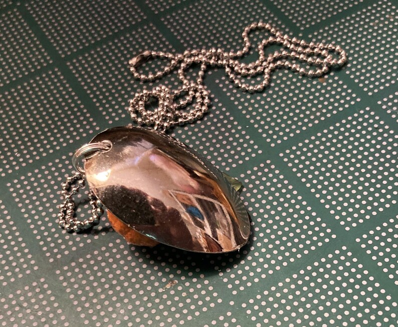 May include: A silver spoon pendant necklace with a silver chain. The spoon is shaped like a heart and has a shiny finish.