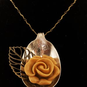 May include: A silver spoon necklace with a brown rose and a gold leaf pendant.