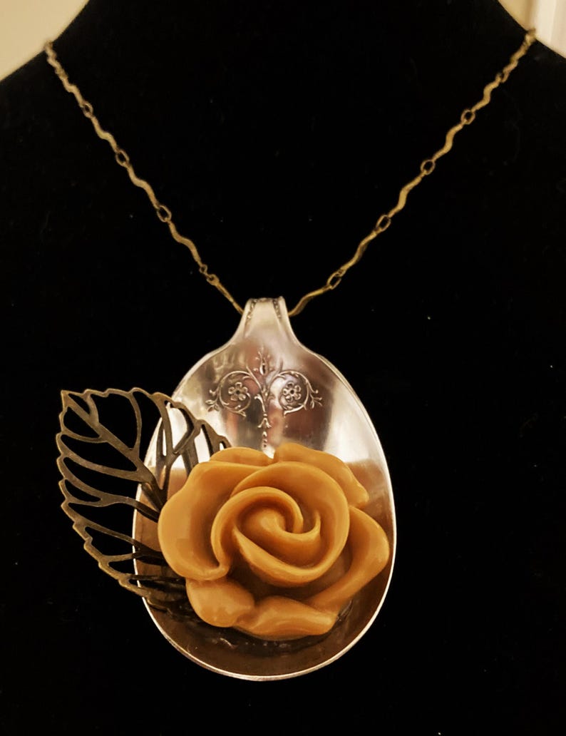 May include: A silver spoon necklace with a brown rose and a gold leaf pendant.