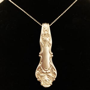 Puede incluir: Un collar de plata con un colgante hecho de una cuchara de plata vintage. La cuchara tiene un dise&ntilde;o adornado con un motivo de hojas.