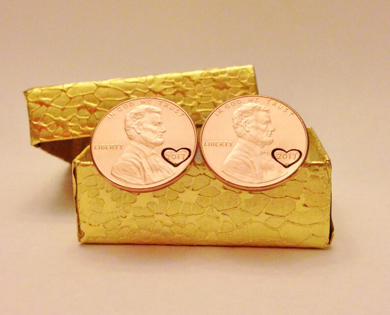 May include: Two copper penny cufflinks with a heart design and the year 2017 engraved on each. The cufflinks are in a small gold box.