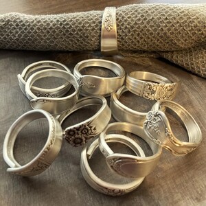 Puede incluir: Un juego de nueve anillos de servilleta de plata hechos con cubiertos reutilizados. Cada anillo presenta un dise&ntilde;o floral &uacute;nico y est&aacute; hecho de una cuchara vintage.