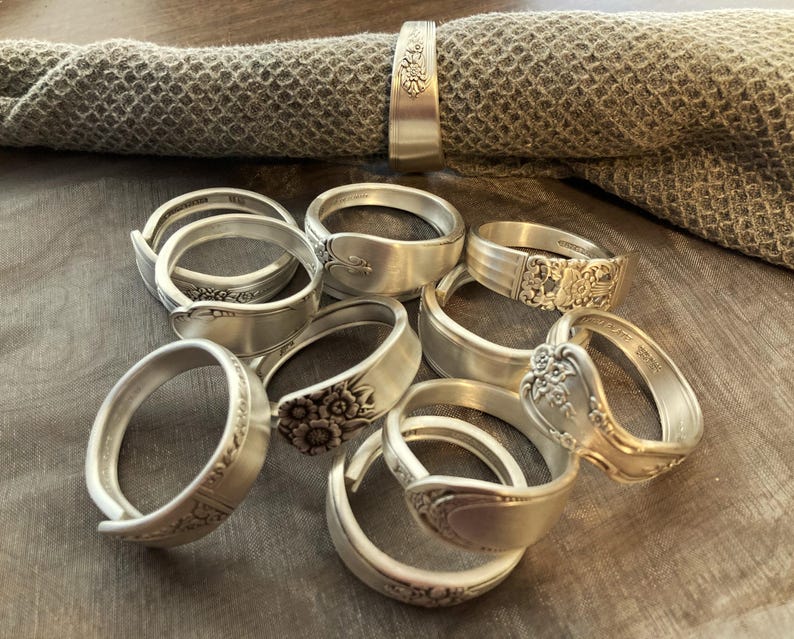 Puede incluir: Un juego de nueve anillos de servilleta de plata hechos con cubiertos reutilizados. Cada anillo presenta un dise&ntilde;o floral &uacute;nico y est&aacute; hecho de una cuchara vintage.