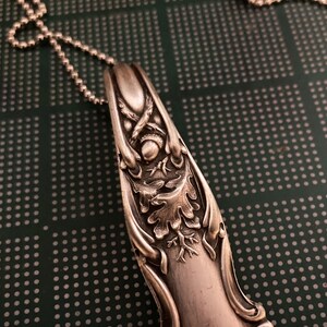 May include: Silver spoon pendant necklace with an ornate design featuring an acorn and oak leaves. The spoon is attached to a silver chain.