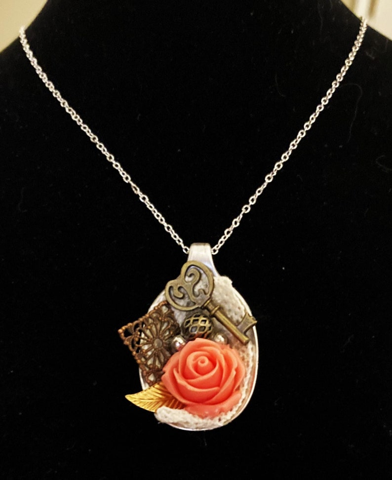 May include: A silver spoon necklace with a pink rose, a key, and other decorative elements.