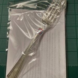 Op de afbeelding: Een zilveren vork met een decoratief ontwerp op de steel. De vork heeft de woorden "Forking Love You" gegraveerd op de steel.