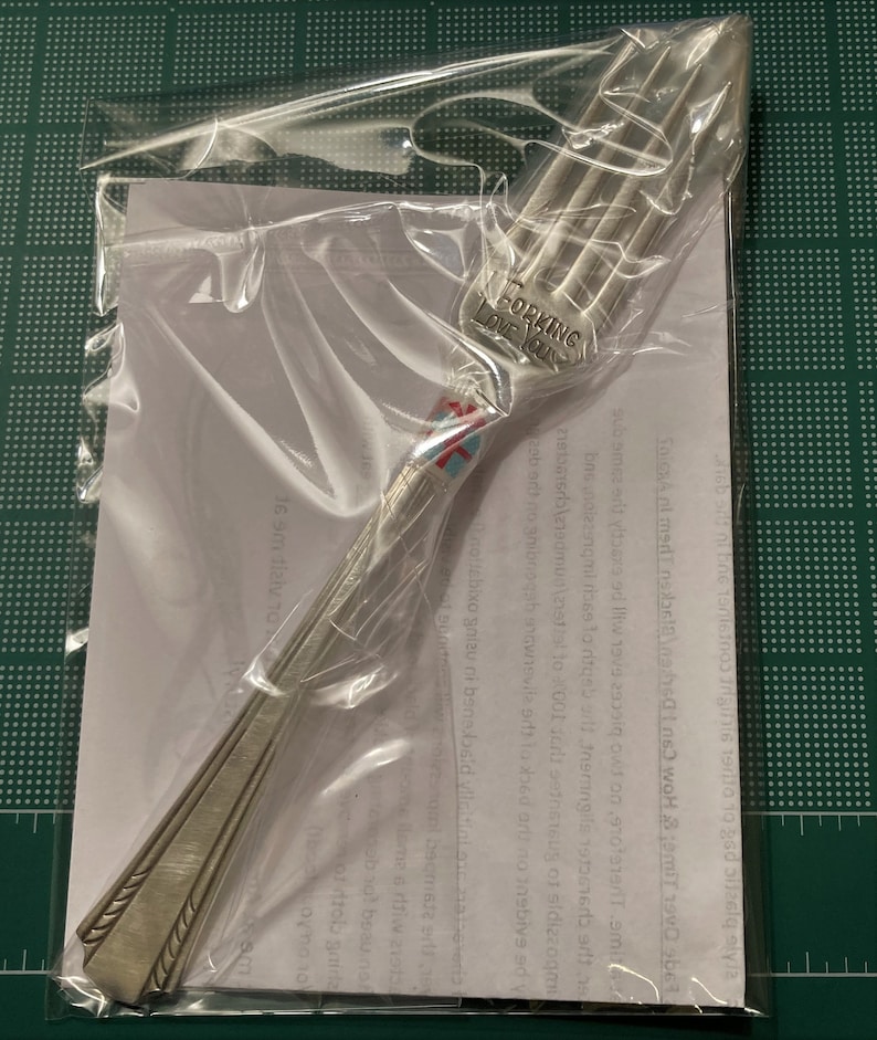 Op de afbeelding: Een zilveren vork met een decoratief ontwerp op de steel. De vork heeft de woorden "Forking Love You" gegraveerd op de steel.